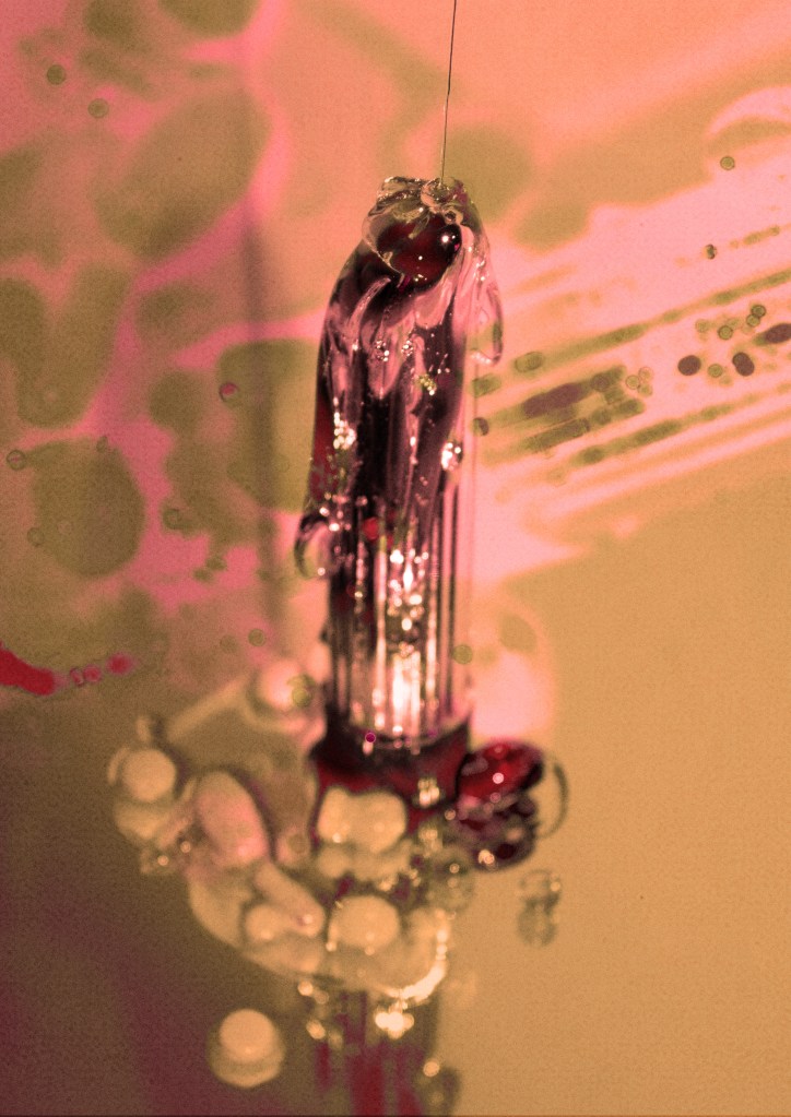 A green-and-pink-tinted photograph of a dildo being covered in thick silicone lube.